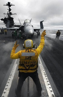 Crew member signaling a fighter jet on an aircraft carrier